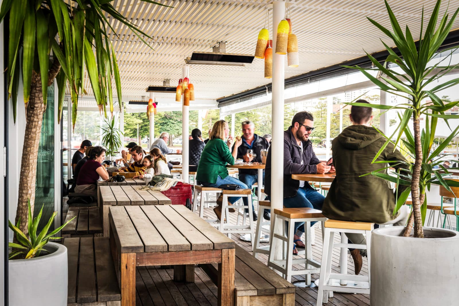 Busy outdoor bar and dining area with potted plants in foreground